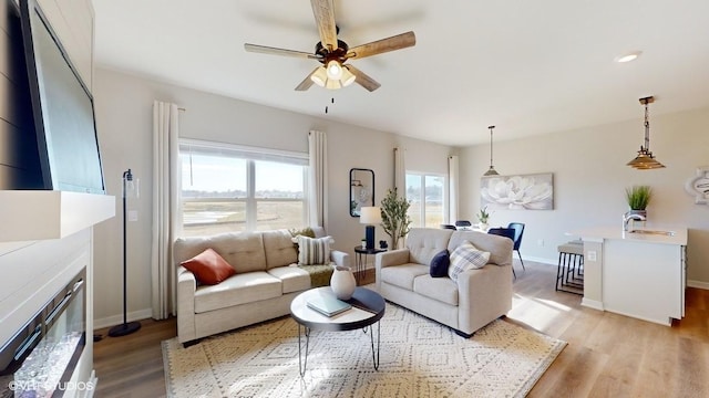 living room featuring a glass covered fireplace, light wood finished floors, baseboards, and ceiling fan