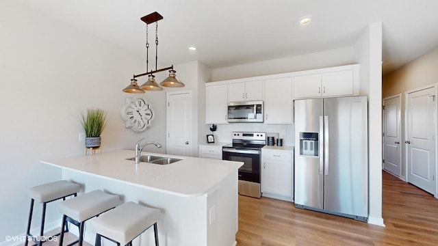kitchen featuring white cabinets, stainless steel appliances, a sink, light wood-style flooring, and a breakfast bar area