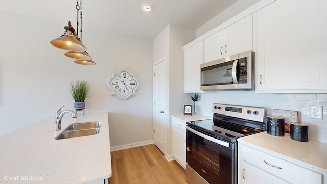 kitchen featuring stainless steel appliances, a sink, light wood-type flooring, decorative backsplash, and white cabinetry