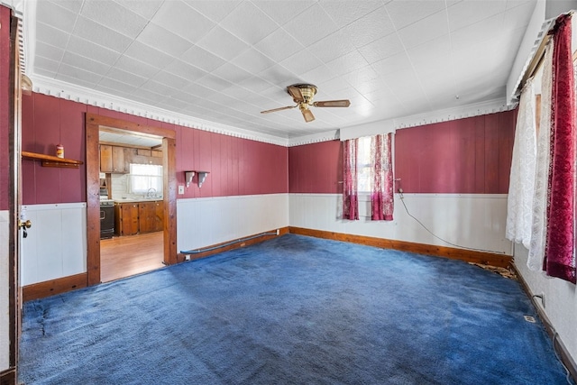 carpeted empty room with a sink, a healthy amount of sunlight, a wainscoted wall, and ceiling fan