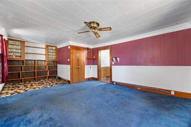 carpeted empty room featuring a wainscoted wall, visible vents, crown molding, and ceiling fan