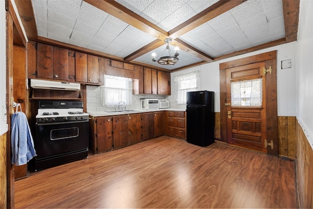 kitchen featuring under cabinet range hood, range with gas stovetop, freestanding refrigerator, an inviting chandelier, and a sink