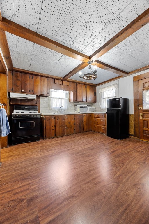 kitchen featuring gas range, brown cabinetry, freestanding refrigerator, and under cabinet range hood