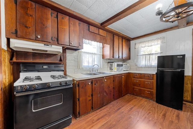 kitchen with under cabinet range hood, light wood-type flooring, range with gas stovetop, freestanding refrigerator, and a sink