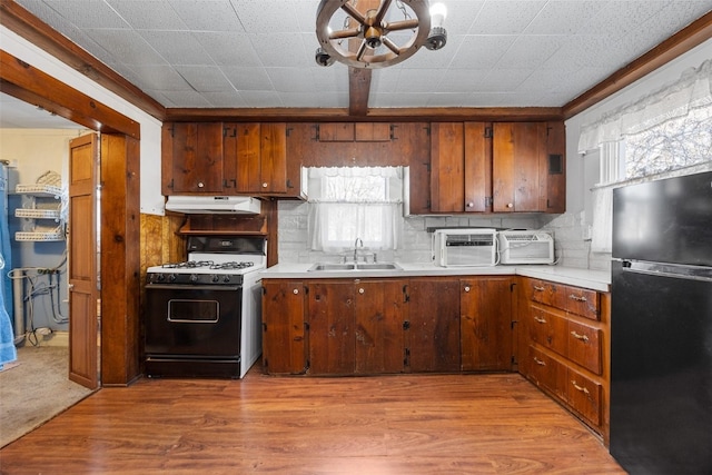 kitchen with under cabinet range hood, a sink, range with gas stovetop, freestanding refrigerator, and an inviting chandelier