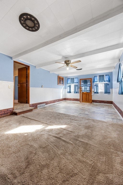 unfurnished living room with visible vents, beam ceiling, a ceiling fan, and carpet flooring