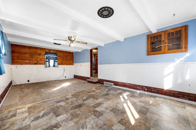 spare room with visible vents, beam ceiling, a wainscoted wall, wood walls, and ceiling fan