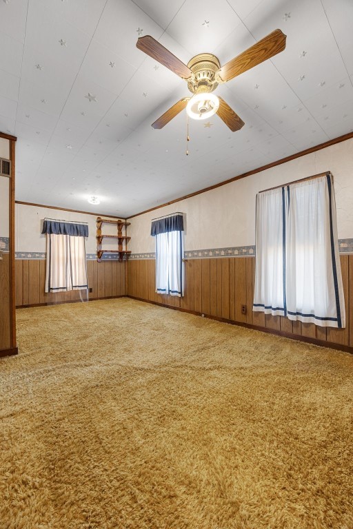 carpeted spare room featuring visible vents, a wainscoted wall, wood walls, and ceiling fan
