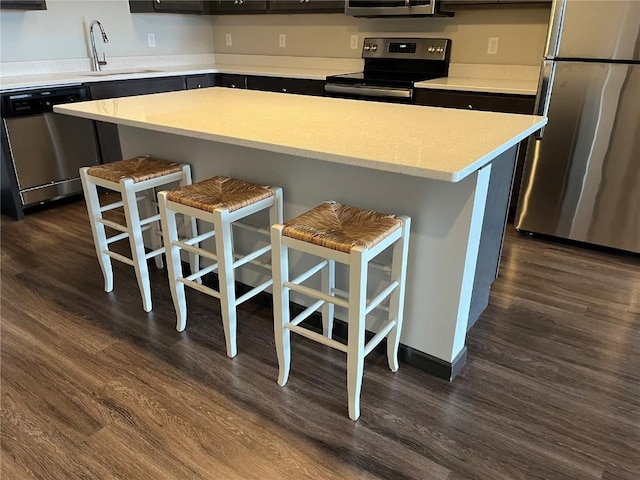 kitchen featuring appliances with stainless steel finishes, a sink, a kitchen bar, dark wood finished floors, and light countertops