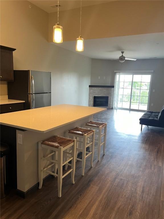 kitchen featuring freestanding refrigerator, dark wood-type flooring, light countertops, ceiling fan, and a fireplace