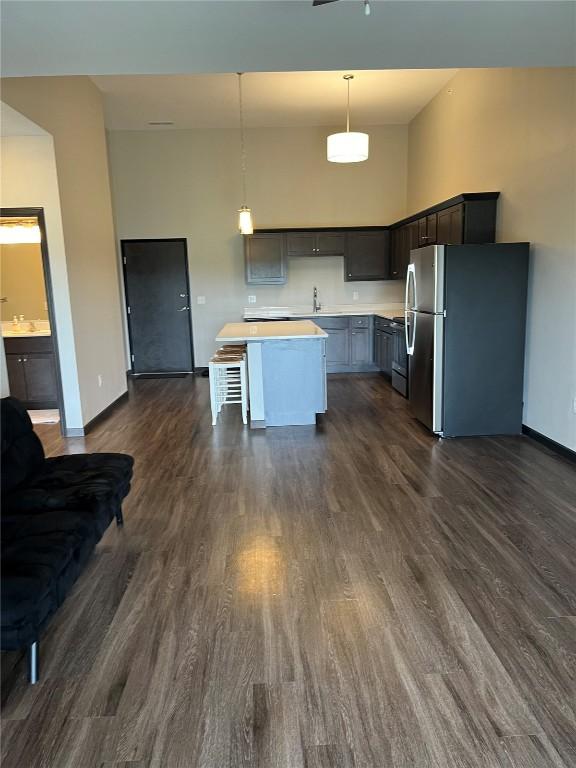 kitchen with freestanding refrigerator, a towering ceiling, baseboards, light countertops, and dark wood-style flooring