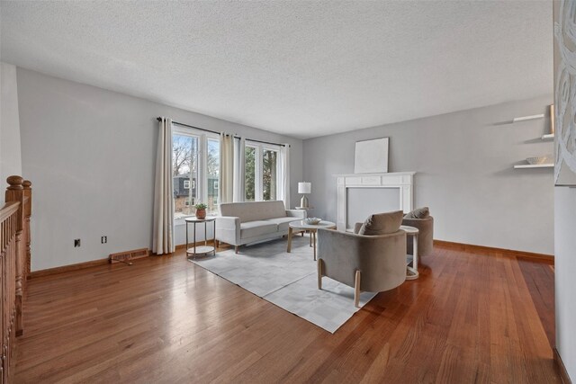 living area featuring visible vents, a textured ceiling, baseboards, and wood finished floors