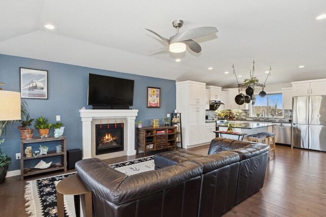 living area with recessed lighting, a warm lit fireplace, dark wood-style floors, and a ceiling fan