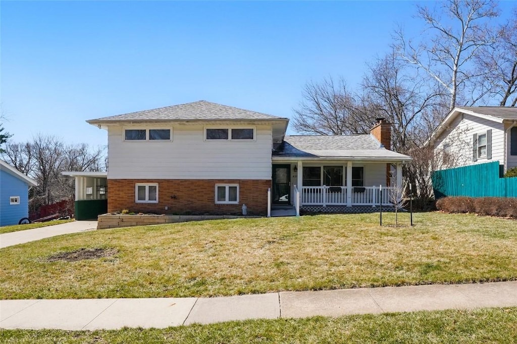 view of front of property featuring brick siding, a porch, a chimney, and a front yard