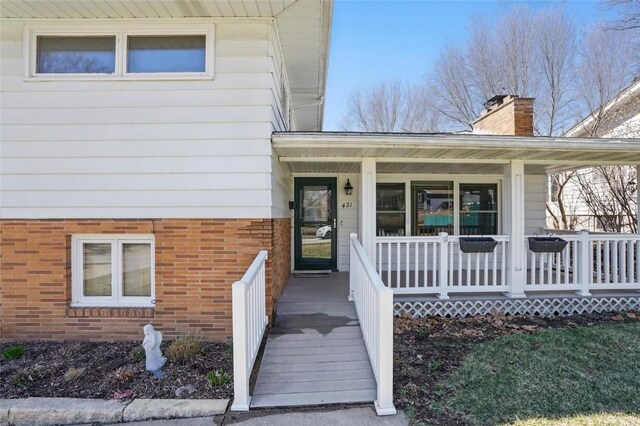 property entrance featuring brick siding, covered porch, and a chimney