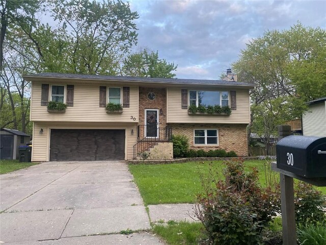 bi-level home with concrete driveway, an attached garage, a front yard, brick siding, and a chimney