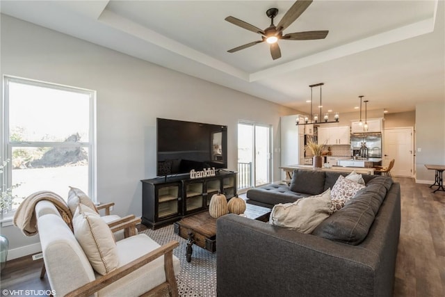living room featuring a tray ceiling, dark wood-style flooring, baseboards, and a ceiling fan