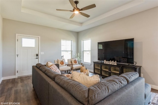 living room with dark wood-style floors, baseboards, a ceiling fan, and a raised ceiling