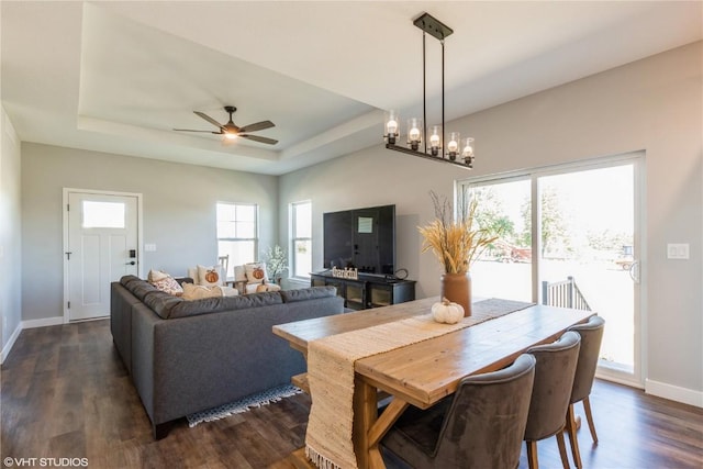 dining area featuring dark wood-style floors, ceiling fan, baseboards, and a raised ceiling
