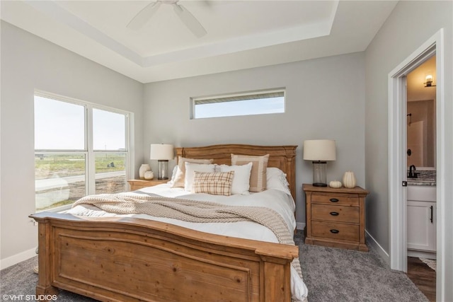 bedroom featuring a tray ceiling, baseboards, ceiling fan, and ensuite bathroom