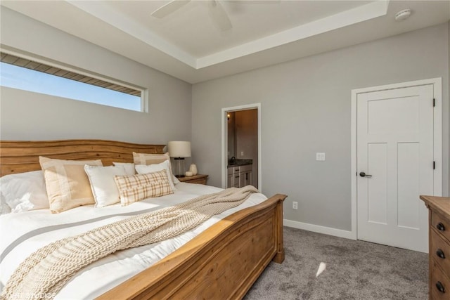 bedroom featuring ensuite bathroom, baseboards, a ceiling fan, a tray ceiling, and light colored carpet