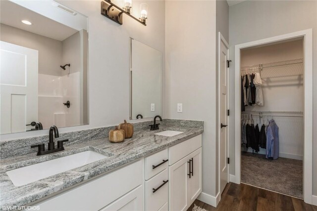 full bathroom with a sink, a walk in closet, a shower, and wood finished floors