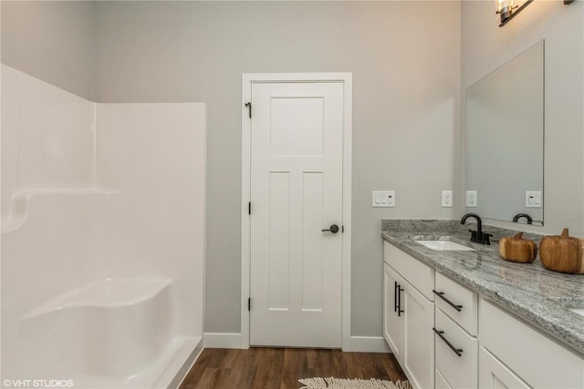 bathroom featuring baseboards, double vanity, walk in shower, a sink, and wood finished floors
