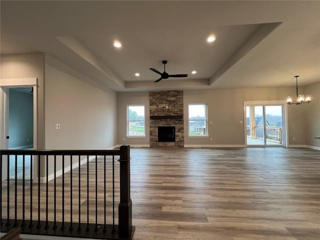 unfurnished living room with ceiling fan with notable chandelier, wood finished floors, a fireplace, a raised ceiling, and baseboards