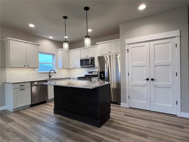 kitchen with a center island, a sink, wood finished floors, backsplash, and appliances with stainless steel finishes