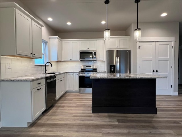kitchen with a sink, light stone countertops, appliances with stainless steel finishes, a kitchen island, and tasteful backsplash