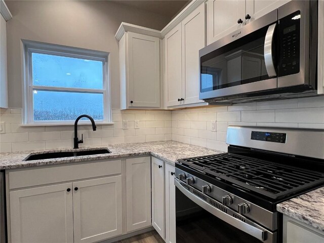 kitchen featuring backsplash, white cabinets, appliances with stainless steel finishes, and a sink