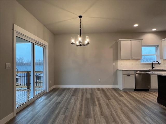 kitchen featuring tasteful backsplash, dark wood-type flooring, light stone counters, dishwasher, and an inviting chandelier