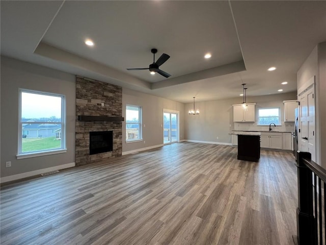 unfurnished living room with light wood-style flooring, baseboards, a sink, ceiling fan with notable chandelier, and a raised ceiling