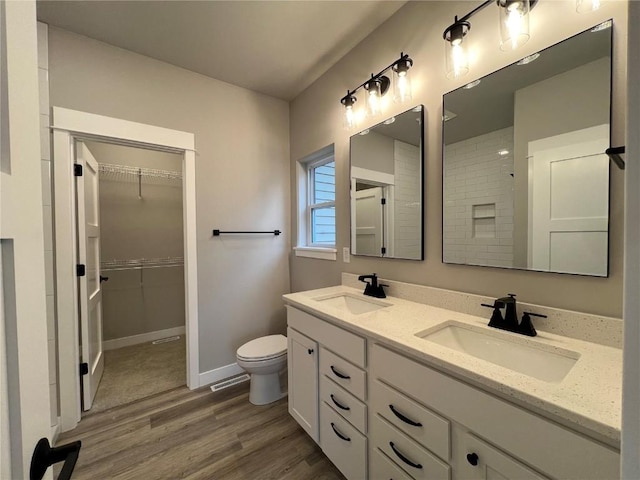full bathroom with a sink, double vanity, toilet, and wood finished floors