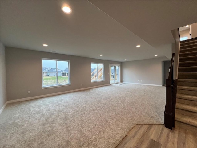unfurnished living room featuring baseboards, stairs, light carpet, and recessed lighting