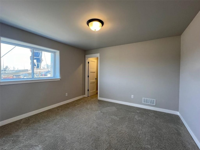 spare room with dark colored carpet, baseboards, and visible vents