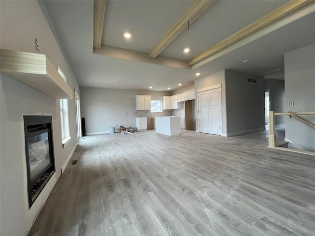 unfurnished living room with a tray ceiling, recessed lighting, light wood-type flooring, and a glass covered fireplace
