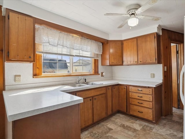kitchen featuring brown cabinetry, ceiling fan, a sink, and light countertops