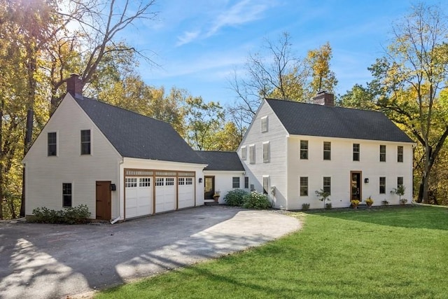 colonial inspired home featuring a chimney, aphalt driveway, a front lawn, a shingled roof, and a garage