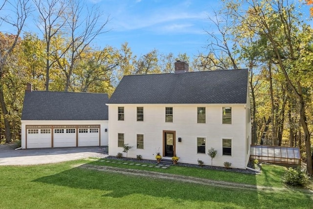 colonial inspired home with a front yard, concrete driveway, a chimney, a shingled roof, and a garage