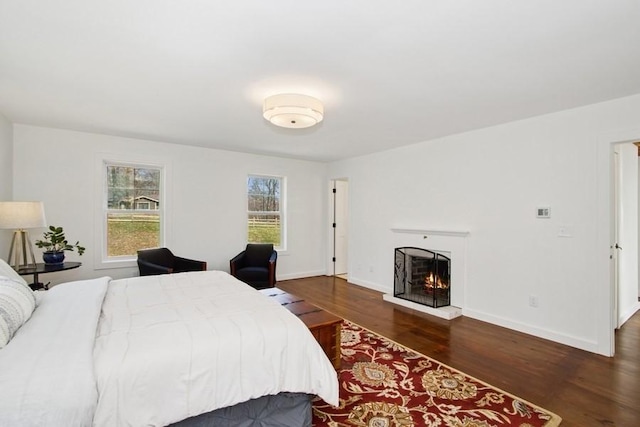 bedroom featuring baseboards, a lit fireplace, and wood finished floors