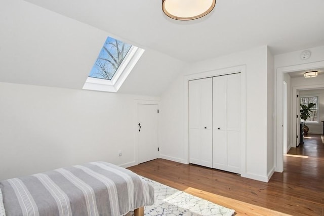 bedroom with baseboards, a closet, wood finished floors, and lofted ceiling with skylight