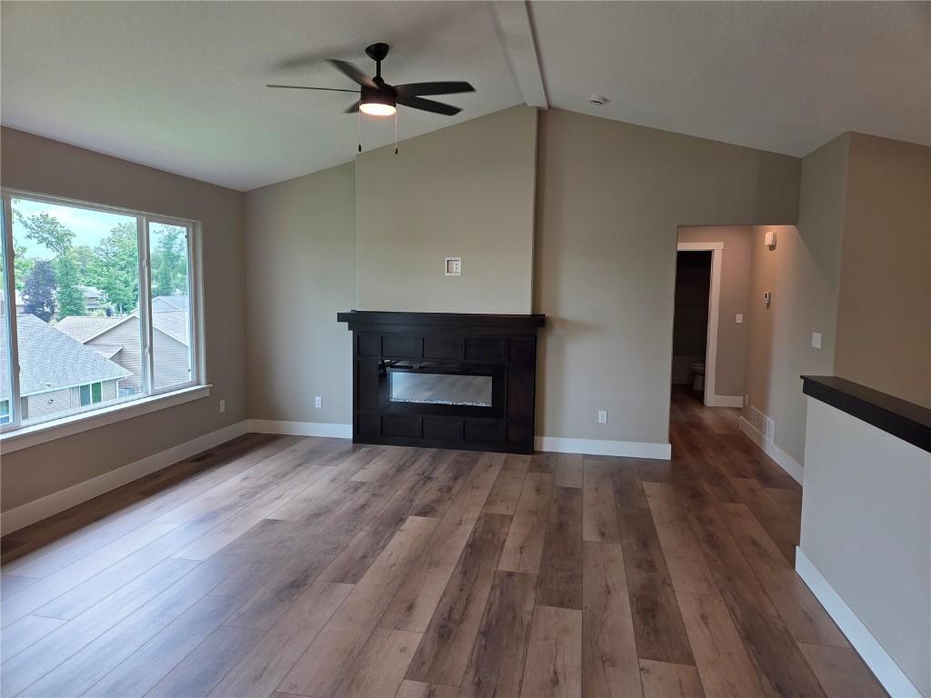 1907 Holly Meadow Ave SW, Cedar Rapids, IA 52404 - unfurnished living room with lofted ceiling, wood finished floors, a ceiling fan, and a glass covered fireplace