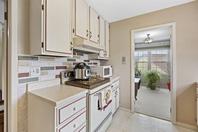 kitchen featuring light countertops, under cabinet range hood, baseboards, white appliances, and decorative backsplash