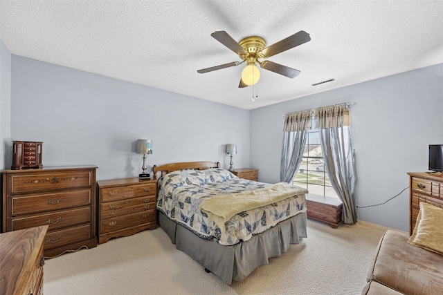 bedroom featuring a textured ceiling, visible vents, a ceiling fan, and light colored carpet