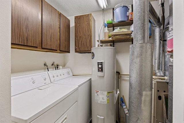 washroom featuring washing machine and clothes dryer, cabinet space, electric water heater, and a textured ceiling