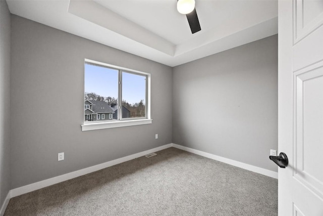 carpeted spare room with baseboards, a tray ceiling, visible vents, and ceiling fan