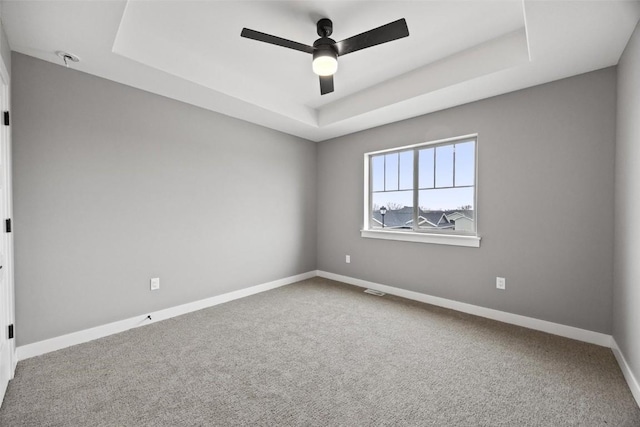 carpeted empty room with a tray ceiling, baseboards, and ceiling fan