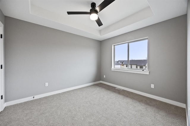 carpeted empty room featuring a ceiling fan, a raised ceiling, baseboards, and visible vents