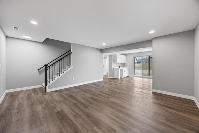 unfurnished living room with recessed lighting, dark wood-type flooring, stairway, and baseboards